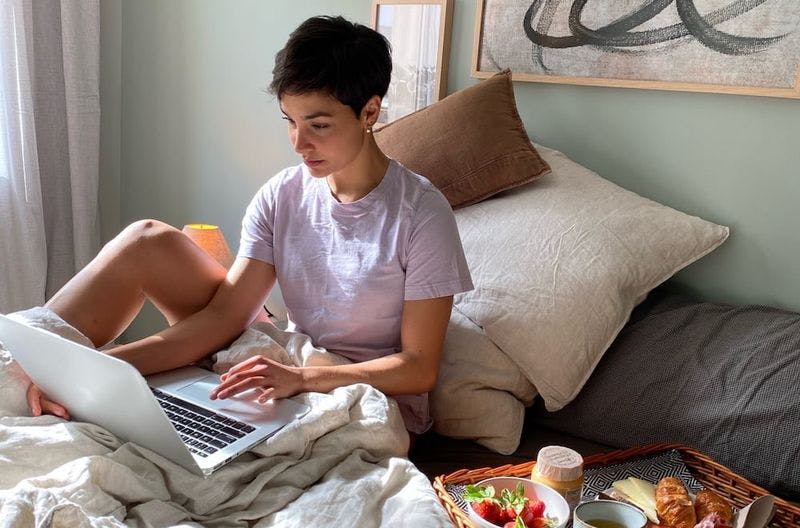 Woman working on a computer in bed with food on the side 
