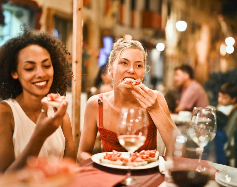 two women eating food with wine