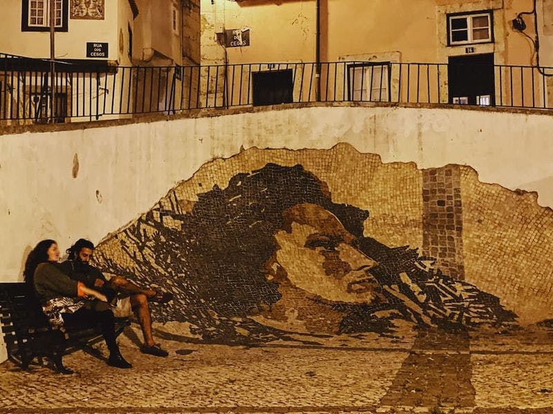 Two people sitting by mural in Lisbon at night